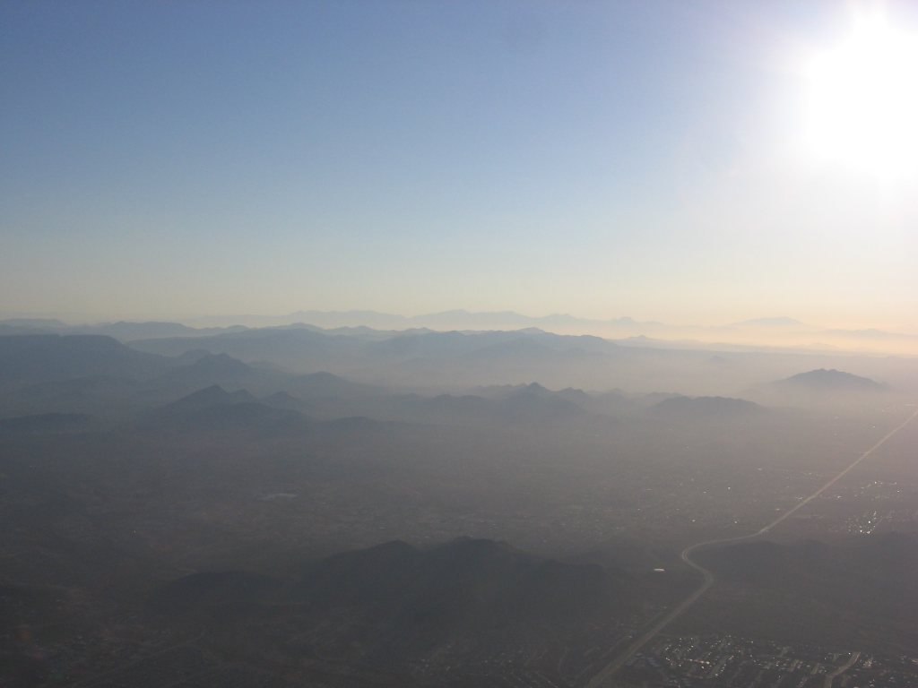 Photograph of a hazy blue sky and mountain peaks coming though fog as the sun breaks though in the early morning sky.