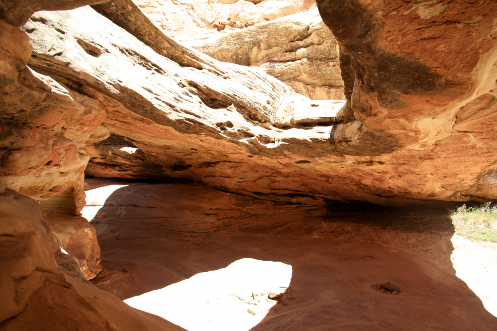 Red rock cave with a large hole in the top that the sun is shining through.